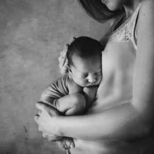 A touching black and white image of a mother gently holding her sleeping newborn close.