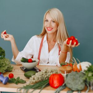 Healthy lifestyle concept with woman holding tomatoes and surrounded by fresh vegetables in a studio setting.